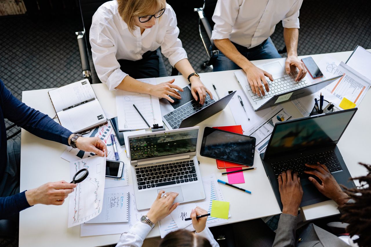 Vue plongeante d’une équipe d’entreprise collaborant avec des ordinateurs portables et des documents.